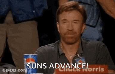 A Man With A Beard Is Sitting At A Table With A Pepsi Can And A Sign That Says Suns Advance . GIF