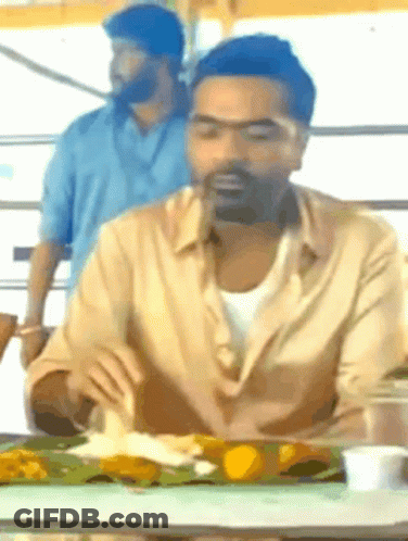 A Man With A Beard Is Sitting At A Table With A Plate Of Food In Front Of Him GIF
