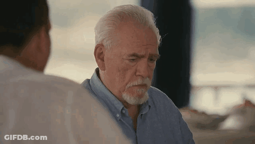 A Man With A Beard Is Sitting At A Table With Another Man . GIF