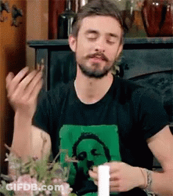 A Man With A Beard Is Sitting At A Table With His Eyes Closed And A Candle In His Hand . GIF