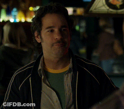 A Man With A Beard Is Sitting At A Table With His Eyes Closed In A Dark Room . GIF