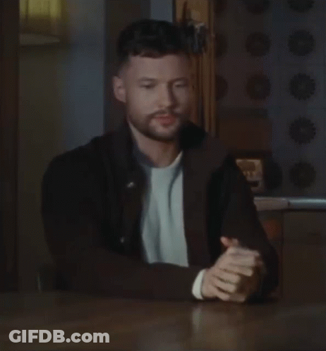 A Man With A Beard Is Sitting At A Table With His Hands Folded In Prayer . GIF
