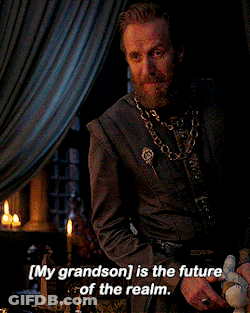 A Man With A Beard Is Sitting At A Table With The Words " My Grandson Is The Future Of The Realm " Above Him GIF
