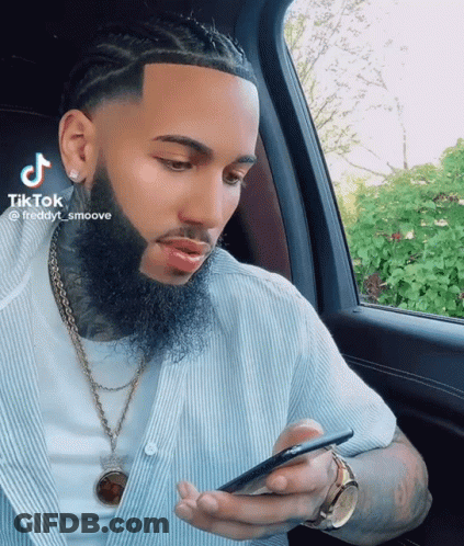 A Man With A Beard Is Sitting In A Car And Looking At His Phone GIF