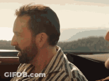 A Man With A Beard Is Sitting In A Car Looking Out The Window . GIF