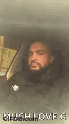 A Man With A Beard Is Sitting In A Car With The Words `` Much Love G '' Written On The Screen . GIF
