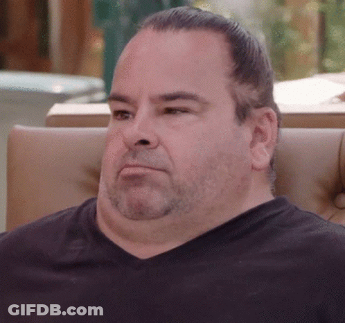 A Man With A Beard Is Sitting In A Chair And Looking At The Camera GIF