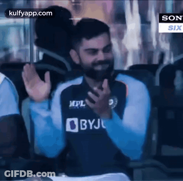 A Man With A Beard Is Sitting In A Chair And Waving His Hands In The Air . GIF