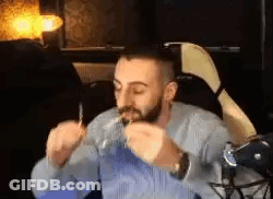 A Man With A Beard Is Sitting In A Chair Eating A Sandwich . GIF