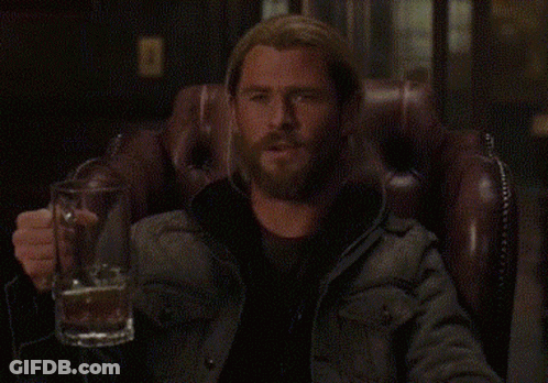 A Man With A Beard Is Sitting In A Chair Holding A Beer Mug . GIF
