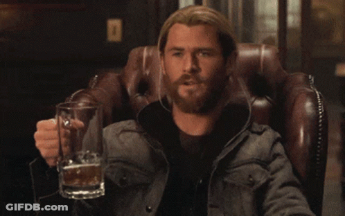 A Man With A Beard Is Sitting In A Chair Holding A Glass Of Beer GIF