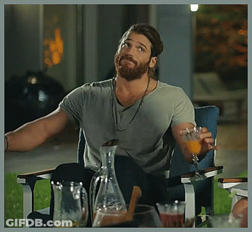 A Man With A Beard Is Sitting In A Chair Holding A Glass Of Orange Juice . GIF