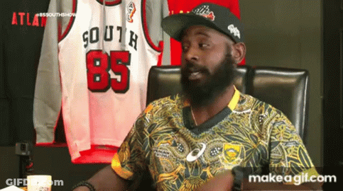 A Man With A Beard Is Sitting In A Chair In Front Of A Display Of Jerseys . GIF