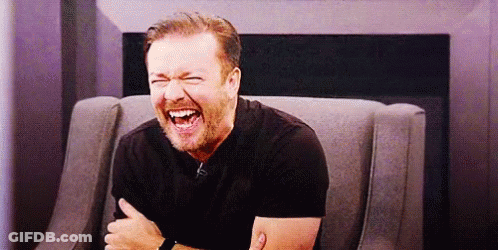 A Man With A Beard Is Sitting In A Chair Laughing With His Arms Crossed . GIF