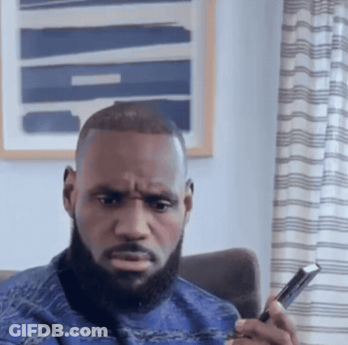 A Man With A Beard Is Sitting In A Chair Looking At A Cell Phone GIF