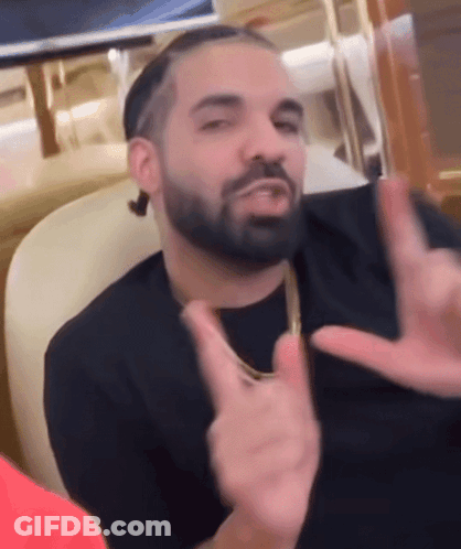 A Man With A Beard Is Sitting In A Chair Making A Peace Sign With His Hands GIF