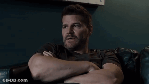 A Man With A Beard Is Sitting In A Chair With His Arms Crossed GIF