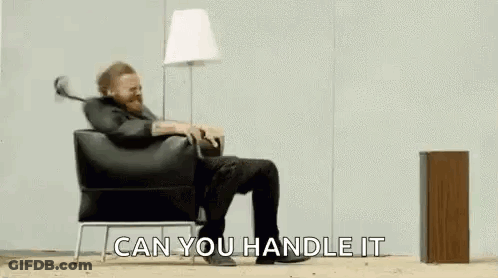 A Man With A Beard Is Sitting In A Chair With His Legs Crossed And A Lamp . GIF