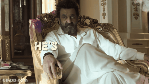 A Man With A Beard Is Sitting In A Chair With The Word He 'S On His Shirt GIF