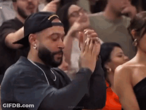 A Man With A Beard Is Sitting In A Crowd Of People Clapping Their Hands . GIF