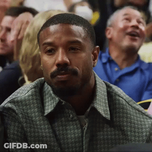 A Man With A Beard Is Sitting In A Crowd Watching A Basketball Game . GIF