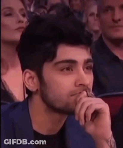 A Man With A Beard Is Sitting In A Crowd With His Hand To His Mouth . GIF