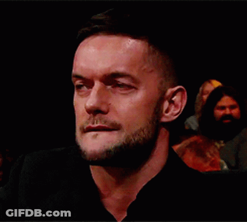 A Man With A Beard Is Sitting In A Dark Room And Looking At The Camera . GIF