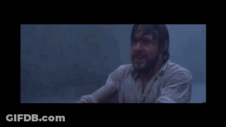 A Man With A Beard Is Sitting In A Dark Room Looking At Something GIF