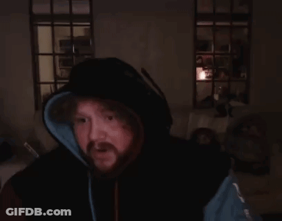 A Man With A Beard Is Sitting In A Dark Room With His Hands Folded . GIF