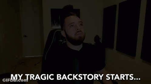 A Man With A Beard Is Sitting In A Dark Room With The Words My Tragic Backstory Starts Behind Him GIF