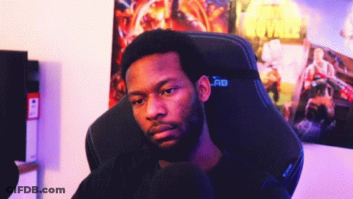 A Man With A Beard Is Sitting In A Gaming Chair In Front Of A Poster Of Battle Royale GIF