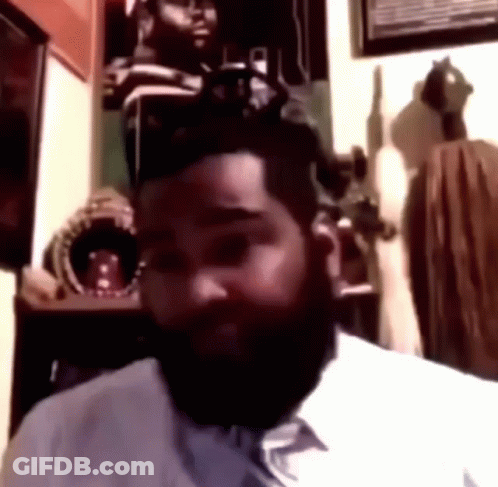 A Man With A Beard Is Sitting In A Room Looking At The Camera GIF