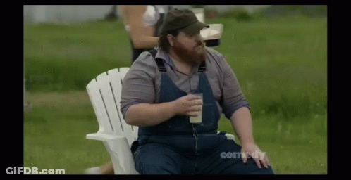 A Man With A Beard Is Sitting In A White Chair Holding A Glass Of Milk GIF