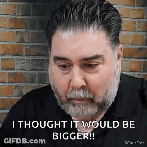 A Man With A Beard Is Sitting In Front Of A Brick Wall . GIF