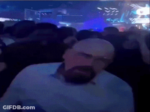 A Man With A Beard Is Sitting In Front Of A Crowd In A Club . GIF