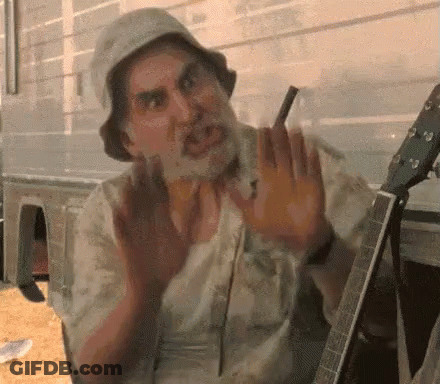 A Man With A Beard Is Sitting In Front Of A Guitar . GIF