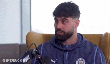 A Man With A Beard Is Sitting In Front Of A Microphone . GIF