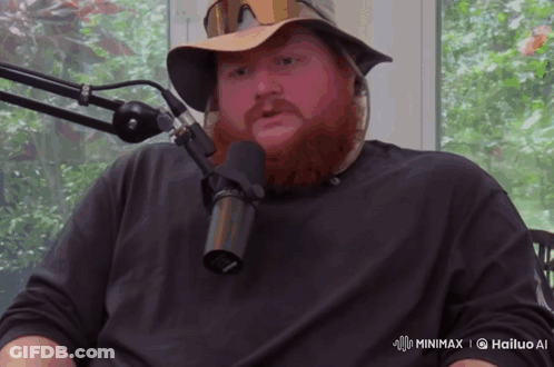 A Man With A Beard Is Sitting In Front Of A Microphone That Says Hailuo Ai On The Bottom Right GIF