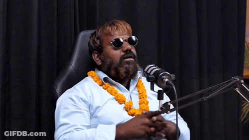 A Man With A Beard Is Sitting In Front Of A Microphone Wearing Sunglasses GIF