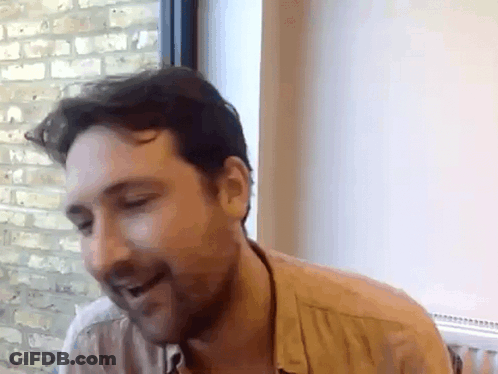 A Man With A Beard Is Sitting In Front Of A Window . GIF