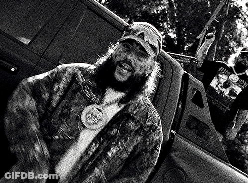 A Man With A Beard Is Sitting In The Back Of A Truck With A Gun . GIF