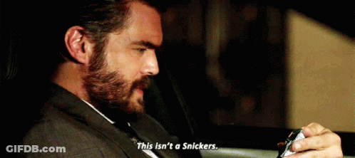 A Man With A Beard Is Sitting In The Back Seat Of A Car Holding A Snickers Bar . GIF
