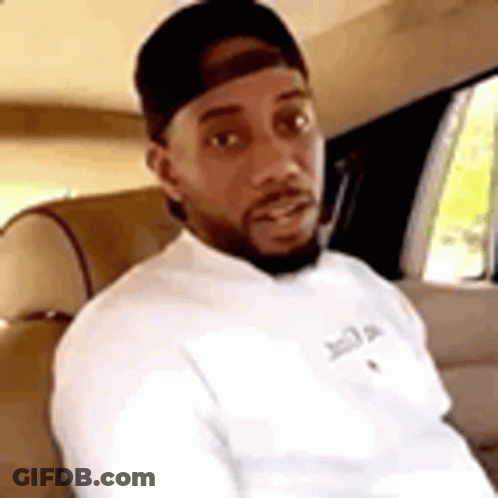 A Man With A Beard Is Sitting In The Back Seat Of A Car Wearing A Hat And A White Shirt . GIF