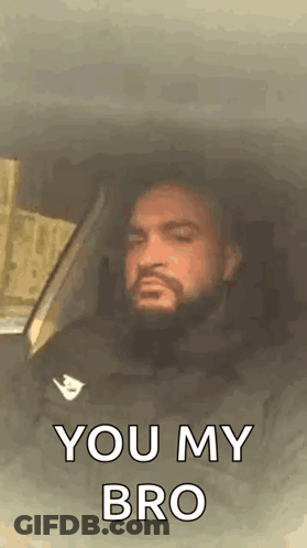 A Man With A Beard Is Sitting In The Driver 'S Seat Of A Car . GIF