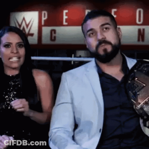 A Man With A Beard Is Sitting Next To A Woman In Front Of A Sign That Says W GIF