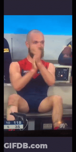 A Man With A Beard Is Sitting On A Bench With His Legs Crossed And His Hands On His Face . GIF
