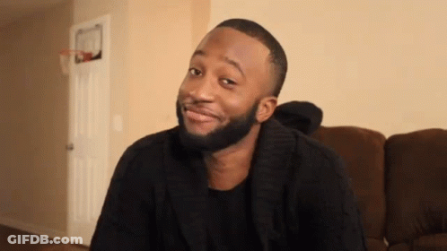 A Man With A Beard Is Sitting On A Couch And Smiling GIF
