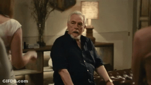 A Man With A Beard Is Sitting On A Couch In A Dark Room GIF