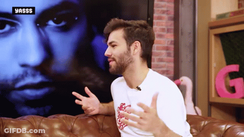 A Man With A Beard Is Sitting On A Couch In Front Of A Yasss Logo GIF