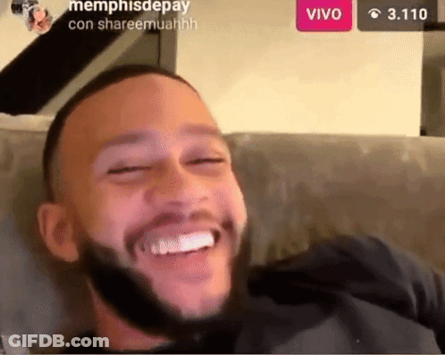 A Man With A Beard Is Sitting On A Couch Smiling GIF